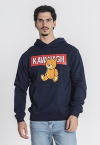 Sudadera azul marino con un gráfico de un oso y el texto "KAVANAGH" en rojo. Fabricada en algodón, cuenta con un bolsillo tipo canguro y puños de canalé.