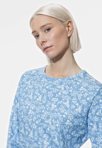 Haut à manches longues bleu clair avec des motifs floraux blancs, col rond et texture douce. Design simple avec une coupe décontractée.