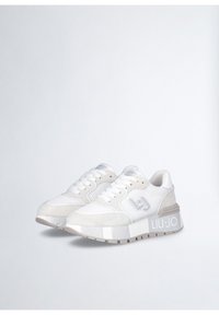 Bílé tenisky vyrobené z prodyšného materiálu a semiše, s robustní podrážkou, šedými akcenty a výrazným logem na boku.