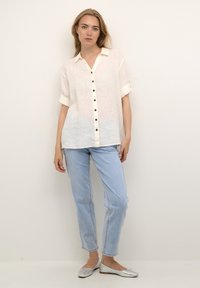 Lys beige linned skjorte med knaplukning, optrukket ærmer og afslappet pasform. Sat sammen med blå jeans og sølvfarvede balletflade.