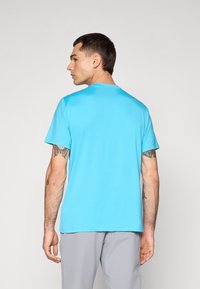 Helles blaues sportliches T-Shirt mit kurzen Ärmeln, Rundhals und glatter Textur. Modell zeigt die Rückansicht, mit Tätowierungen am Arm.