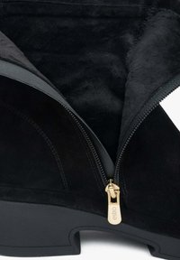 Czarne zamszowe botki za kostkę z złotym zamkiem błyskawicznym, posiadające miękką podszewkę, zaokrąglony nosek i masywną czarną gumową podeszwę.