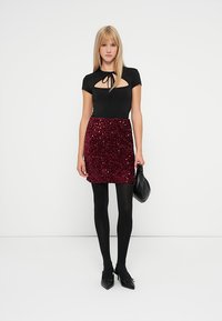 Crna uska majica s izrezom u obliku ključa, u kombinaciji s maroon minicom s paillettes. Crne tajice i crne štikle s oštrim vrhom upotpunjuju izgled.