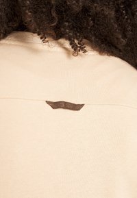 Bežīgs audums ar mīkstu tekstūru, aizmugurē ir neliels br�ūns tagiņš. Dizainā ir vienkārša, tīra silueta.