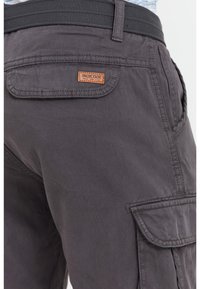 Dark gray cargo pants with flap pockets and a black belt, showing a small "INDICODE" leather brand label on the back pocket.