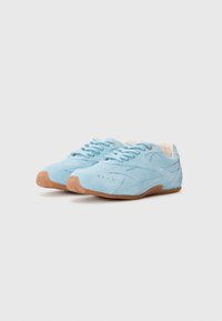 Light blue suede athletic shoes with beige lining, flat rubber sole, and traditional lacing. Features curved stitching and perforated details.