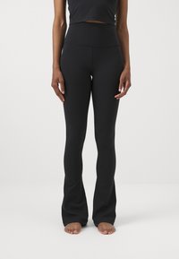 Czarne leggings w kształcie dzwonów wykonane z elastycznego materiału z wysokim pasem, gładką teksturą i minimalną ilością szwów. Idealne do codziennego użytku lub aktywności fizycznej.
