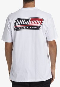 Bílý bavlněný tričko s velkým černým a červeným logem "Billabong" na zadní straně, pod kterým je text "SINCE SEVENTY THREE".