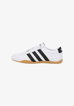 Scarpe da ginnastica bianche con strisce nere, realizzate in materiale sintetico, con suola in gomma e lacci davanti. Design a profilo basso.