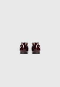 Ballerines en cuir verni bordeaux avec des bouts ronds, des semelles noires fines et des nœuds assortis à l'arrière. Texture lisse et brillante.