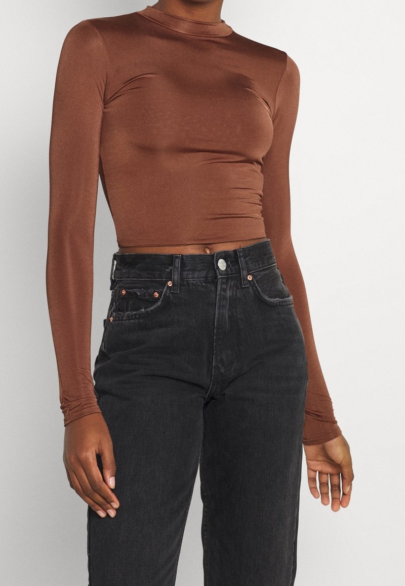 Ruskea pitkähihainen lyhyt paita sileästä kankaasta yhdistettynä korkeavyötäröisiin mustiin farkkuihin, joissa on kontrastitikkaukset ja klassinen viiden taskun malli.