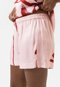 Roze satijnen shorts met een rood abstract patroon, voorzien van een elastische tailleband en zijsplitten voor bewegingsgemak. Gladde textuur.