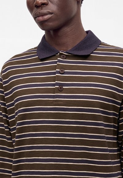 Homme portant un polo à manches longues rayé marron, bleu marine et blanc avec trois boutons et un col bleu marine foncé.