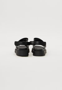 Sandalias negras con un diseño de espalda abierta, que presentan correas anchas y una suela plana. Fabricadas con material suave y con un detalle mínimo.
