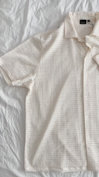 Rövid ujjú, fehér ing, texturált anyagból, kis nyitott szövésekkel és gombos záródással a gallérnál.
