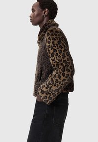 Leparda raksta jaka ar mīkstu, strukturētu audumu, ar augstu apkakli un īsu dizainu. Kombinēta ar melnām džinsa biksēm.