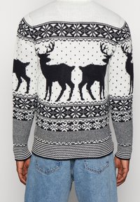 Vit och marinblå stickad tröja med mönster av renar, snöflingor och prickar; ribbade ärmslut och nederkant; texturerad tyg.