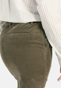 Olijfgroene corduroy broek heeft een rechte pasvorm, zijzakken en details op de achterzak. Gecombineerd met een wit en lichtgrijs gestreept shirt.