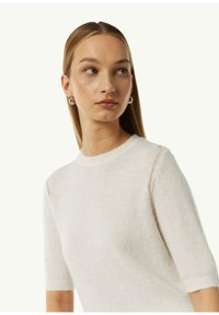 Helles beige Kurzarmpullover aus weichem, strukturiertem Stoff mit rundem Ausschnitt und zarten Strickdetails an den Schultern.