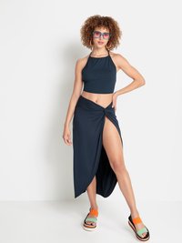 Haut court halter marine et longue jupe portefeuille avec une fente latérale, associée à des sandales colorées et épaisses. Lunettes de soleil claires et surdimensionnées.