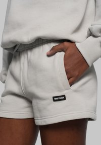 Lichtgrijze katoenen shorts met een elastische tailleband, zijzakken en een zwart logo-patch met "WRSTBHVR" op het onderbeen.
