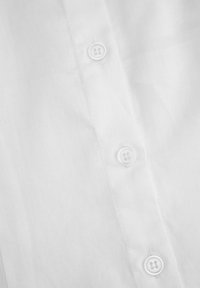 Zbliżenie na białą tkaninę z trzema białymi guzikami przyszytymi w pionowym rzędzie wzdłuż przeszytej listwy.