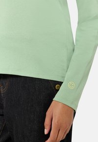 Langarm-Hemd in Mintgrün aus weichem Baumwollmaterial, mit lockerer Passform und einem kleinen gestickten Smiley-Gesicht am Bündchen.