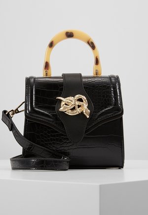 Sort håndtaske med krokodilletekstur, skildpaddehåndtag, gyldent dekorativt spænde og aftagelig skulderrem på hvid overflade.
