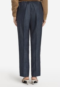 Mörkblå, skräddarsydda byxor med rak passform och bakre veck, tillverkade av texturerat tyg; kombinerade med ljusfärgade, spetsiga klackar.