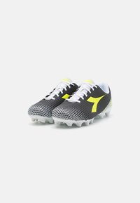 Scarpe da calcio in bianco e nero con un motivo geometrico simile a una rete, dotate di un logo giallo vivace e lacci bianchi, progettate per la trazione.