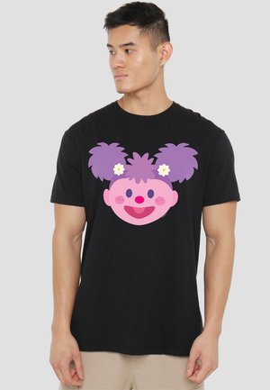 Schwarzes Baumwoll-T-Shirt mit einem großen, stilisierten pinken Gesicht mit lila Zöpfen und weißen Blumen, zentriert auf der Vorderseite.