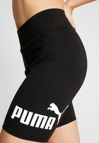 Pantaloni corti neri con cintura alta e grande logo bianco "PUMA" con silhouette di un felino in salto sulla gamba sinistra.