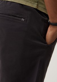 Czarne spodnie o gładkiej fakturze, z boczną kieszenią i ozdobnym przeszyciem. Część stroju noszonego z zieloną bluzką.