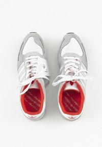 Šedé semišové a bílé síťované tenisky s červeným vnitřkem, se třemi bílými pruhy, bílými šňůrkami a červeným logem Adidas na podrážce.