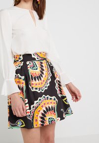 Vit blus med nyckelhålsringning och trumpetärmar, i kombination med en svart kjol med färgglada paisleymönster och livfulla accenter.