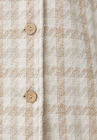 Tissu beige et blanc texturé avec un motif tissé en diagonale comportant deux boutons ronds en bois cousus verticalement.