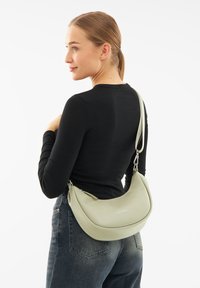 Borsa a spalla verde in pelle con design curvo, texture liscia e branding sottile. Presenta una tracolla regolabile e chiusura con zip.