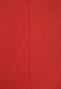 Czerwona bawełniana tkanina o gładkiej fakturze, z widocznymi szwami, które tworzą subtelny wzór. Równomierny kolor bez widocznych akcentów czy elementów metalowych.