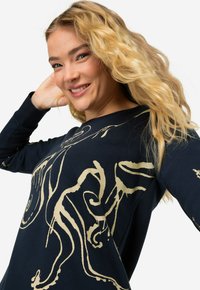 Sweatshirt navy à manches longues avec un motif abstrait doré. Fabriqué en tissu doux, il a une coupe décontractée et une texture subtile.