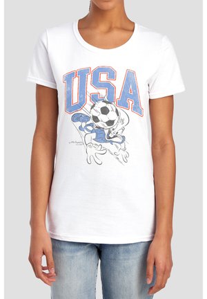 Person trägt ein weißes T-Shirt mit großem blau-rotem Umrisstext "USA" und einer Cartoon-Figur, die einen Fußball köpft.