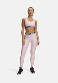 Svetlo roza športni crop top z črnim pasom pod prsmi, ki je v kombinaciji z usklajenimi leginami. Oboje ima gladko, prilegajočo se teksturo. Črni superge.