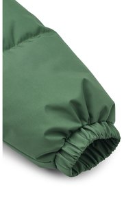 Manche de veste rembourrée verte avec poignet élastique, texture de tissu lisse et détails cousus le long de la couture.