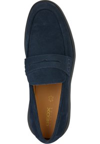 Mocasines de ante azul marino con suela plana, que presentan una correa decorativa en el empeine y sutiles detalles de costura. El interior tiene un forro color camel.