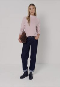 Un pull col roulé rose pâle, un jean en denim foncé retroussé aux poignets, des bottines noires et une pochette marron. Design simple et couleurs neutres.