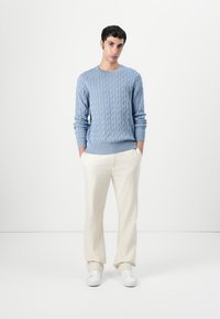 Pulover tricotat de culoare albastru deschis, cu manșete cu nervuri, asortat cu pantaloni de culoare crem și adidași albi. Design simplu, cu textură.