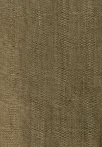 Gros plan d'un tissu tissé grossier vert olive avec une texture en quadrillage visible et des fibres irrégulières.