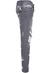 Jeans ajustados grises con tejido desgastado, presentan salpicaduras de pintura blanca en contraste y un detalle de rodilla rasgada. Diseño clásico de cinco bolsillos.