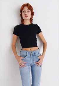 Must musta t-särk, mis on kombineeritud kõrge vöökohaga heledast sinisest džinsist, millel on kaks esimest nuppu, heleda denimitekstuuri ja viie tasku stiil.