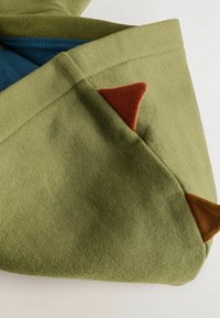 Produit textile vert avec une finition texturée, présentant des accents triangulaires contrastants en rouille et brun près du bord.