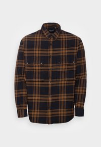 Camicia a maniche lunghe a quadri nera e marrone, con due tasche sul petto, chiusura con bottoni e una texture di tessuto morbido.